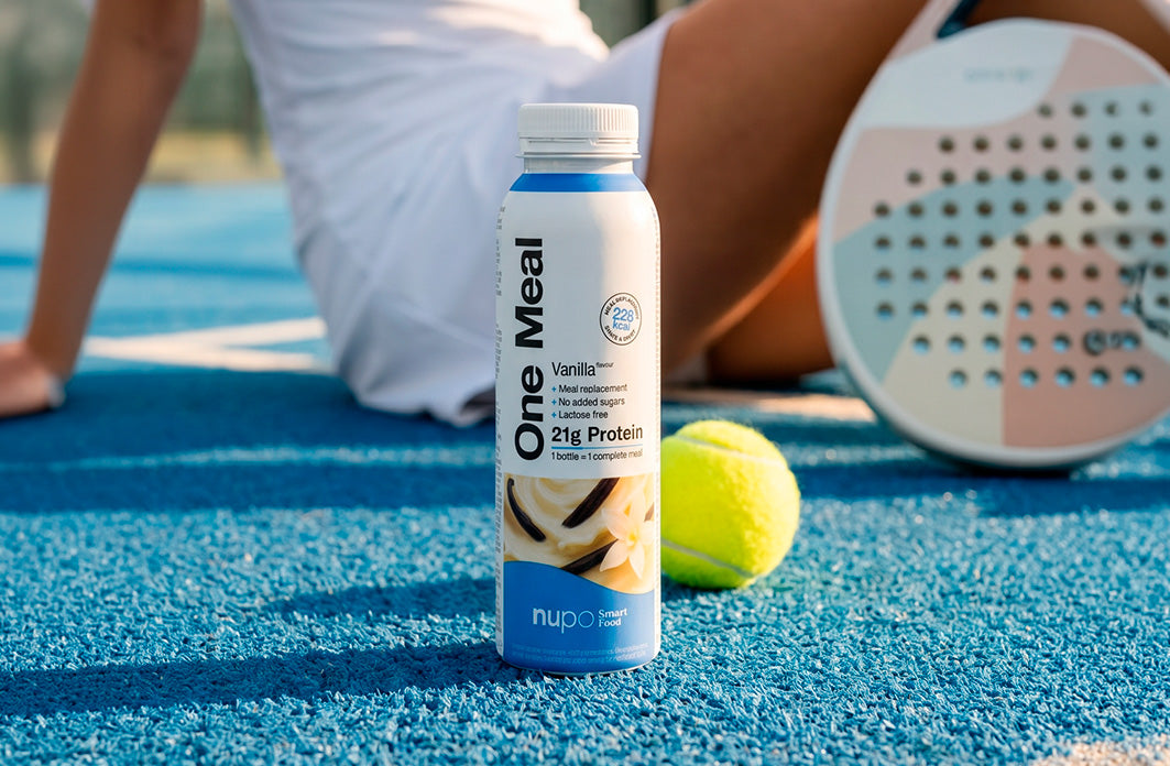 Vanilla protein drink bottle on tennis court, featuring 21g protein, with tennis ball in foreground.