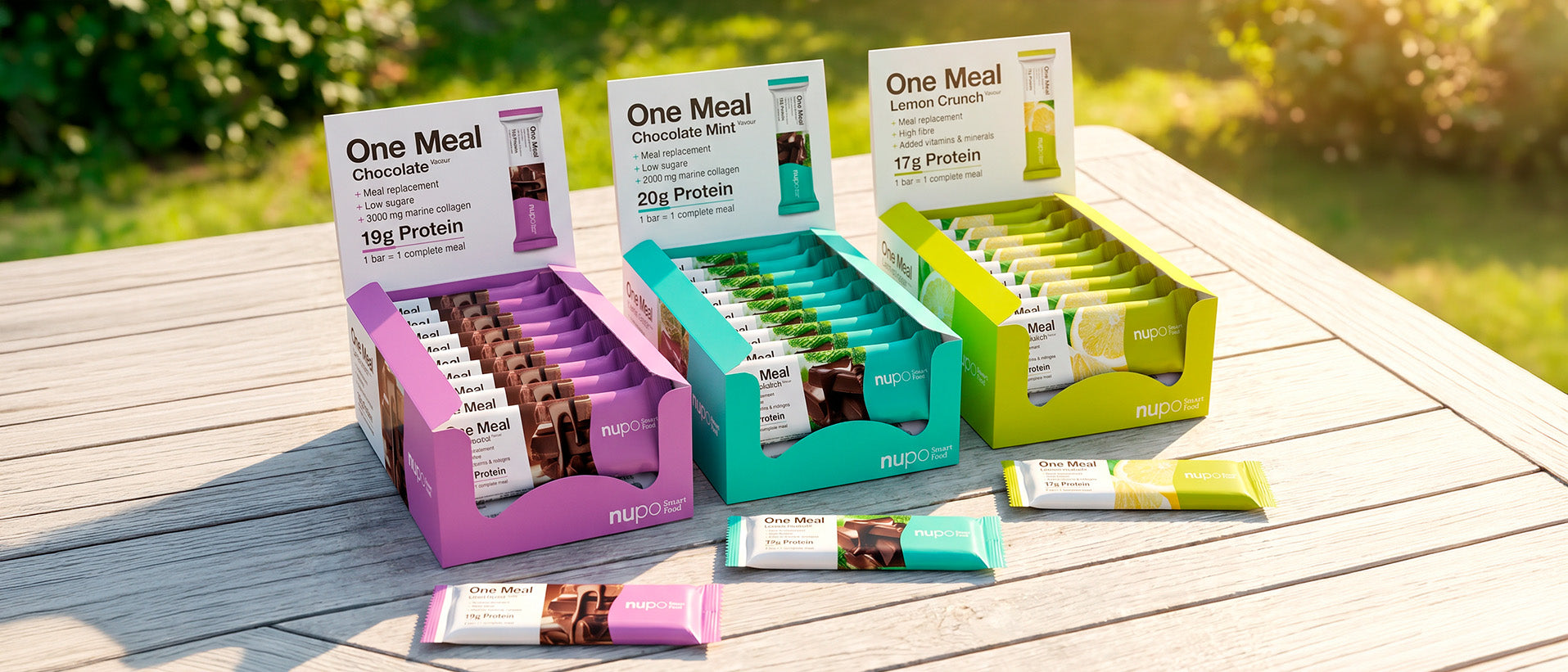 Display of One Meal protein bars in assorted flavors on a sunny table, featuring Chocolate, Lemon Crunch, and Cookies flavors.